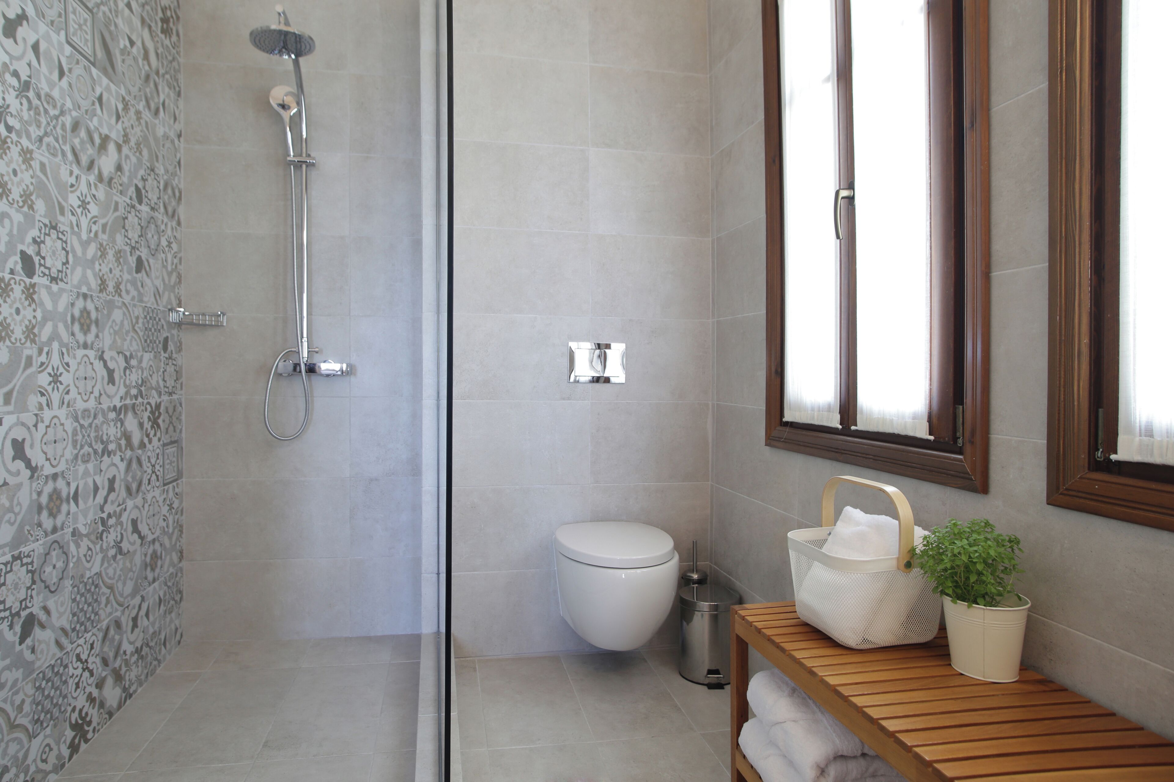 A bathroom with a shower, toilet, and a wooden bench with a plant.