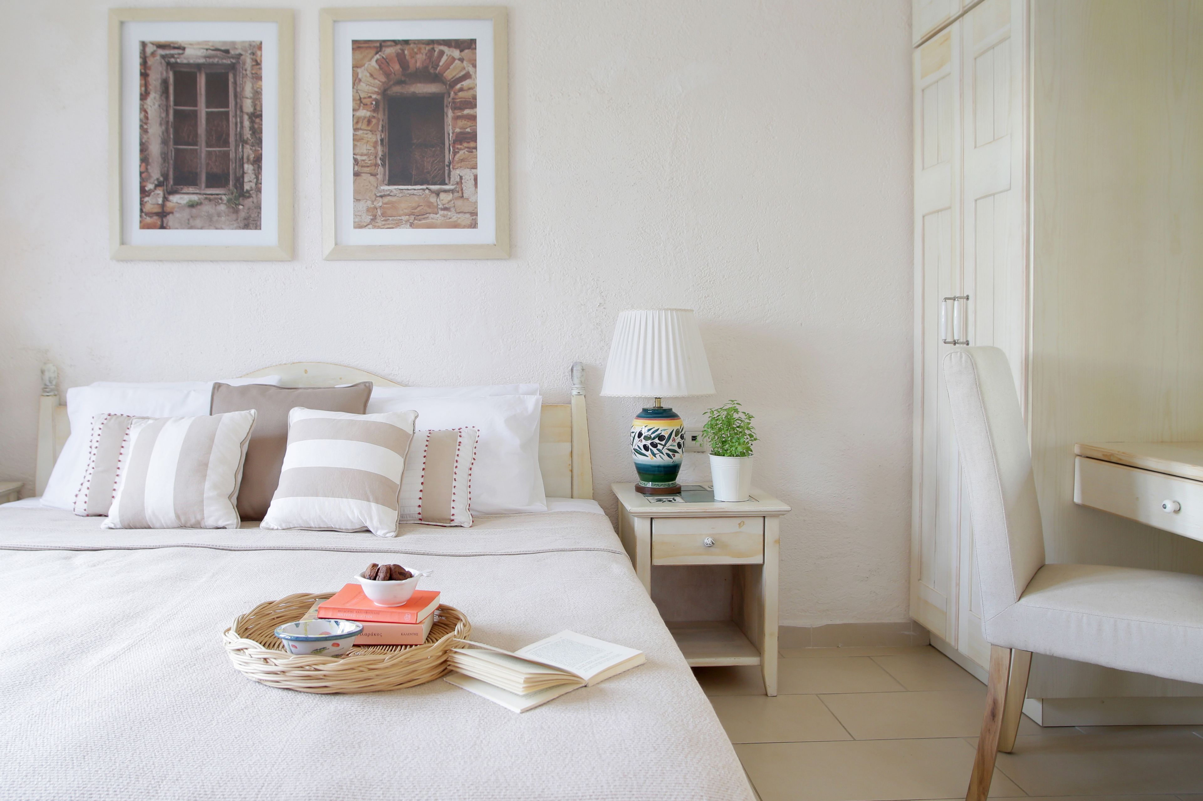 A neatly arranged bedroom with a bed, bedside table, lamp, chair, and two framed pictures on the wall.