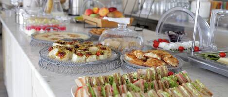 A buffet with various food items including sandwiches, pastries, and fruits.