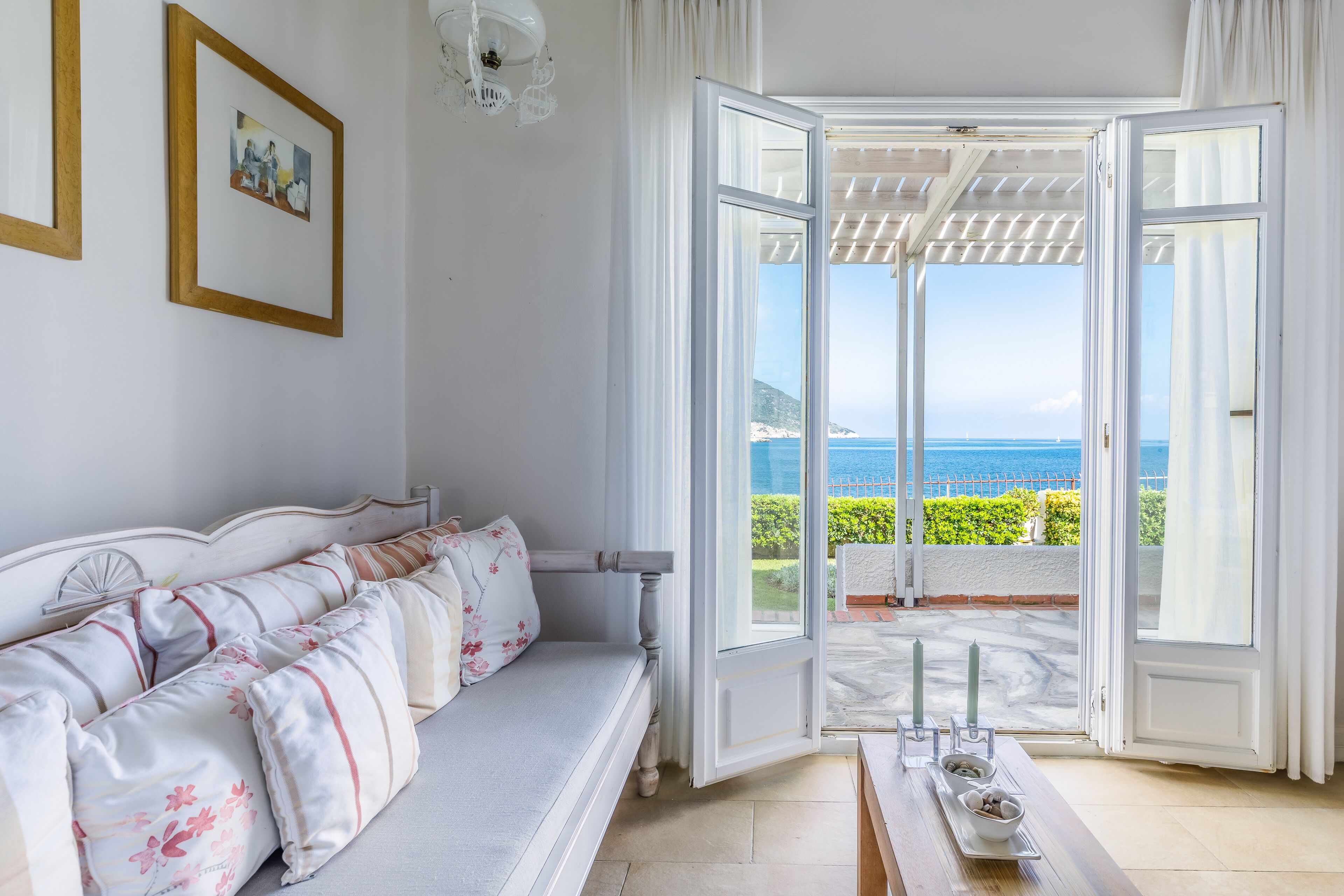 Una habitación con un sofá blanco, una mesa con velas y vistas al mar a través de puertas abiertas.