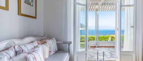 Una habitación con un sofá blanco, una mesa con velas y vistas al mar a través de puertas abiertas.