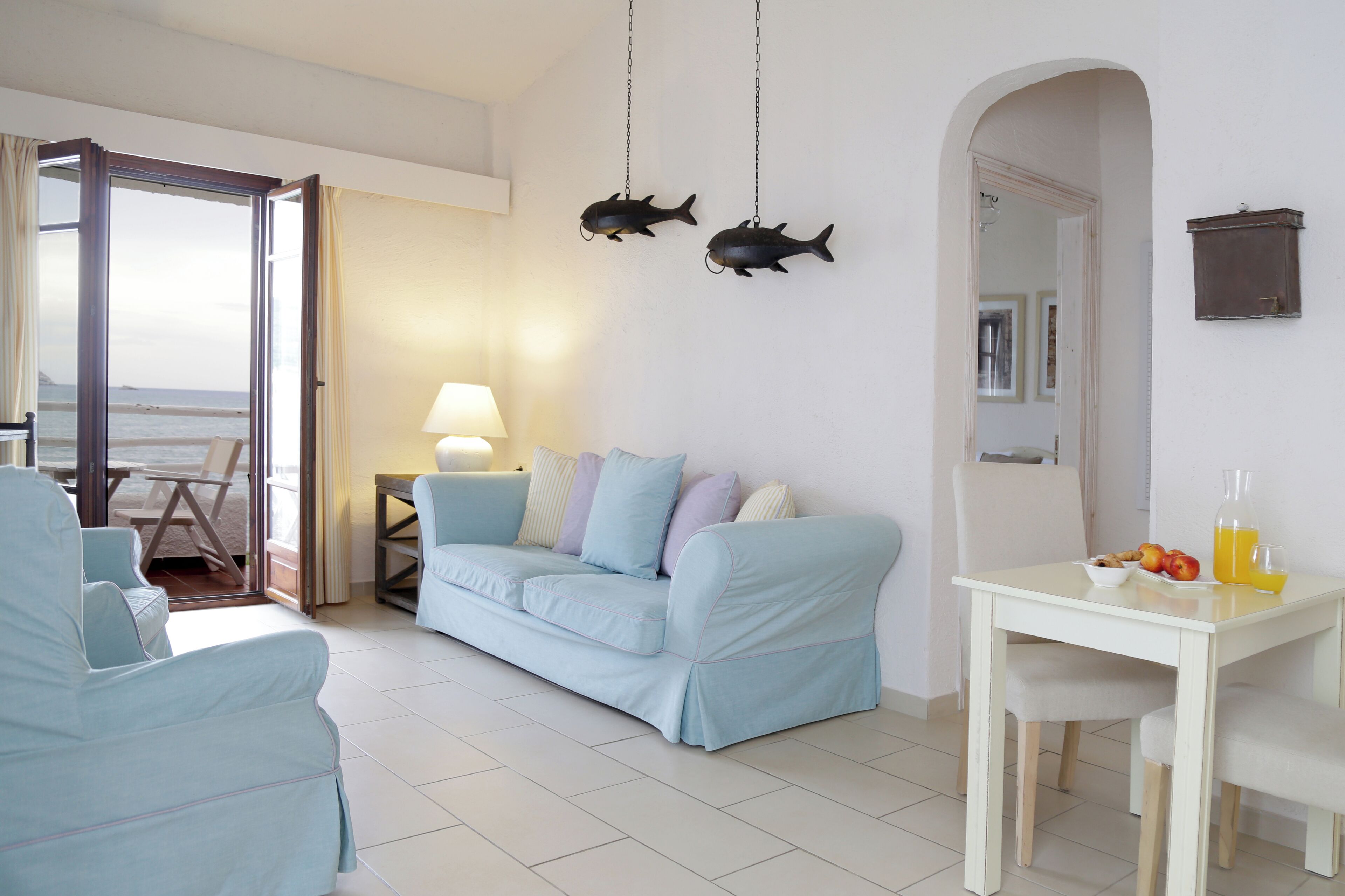 A living room with a light blue sofa, a small table with fruit and drinks, and two hanging fish decorations.