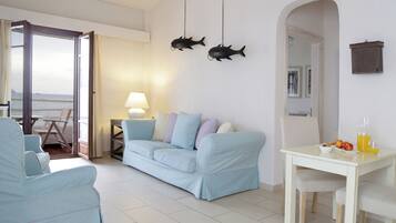 A living room with a light blue sofa, a small table with fruit and drinks, and two hanging fish decorations.