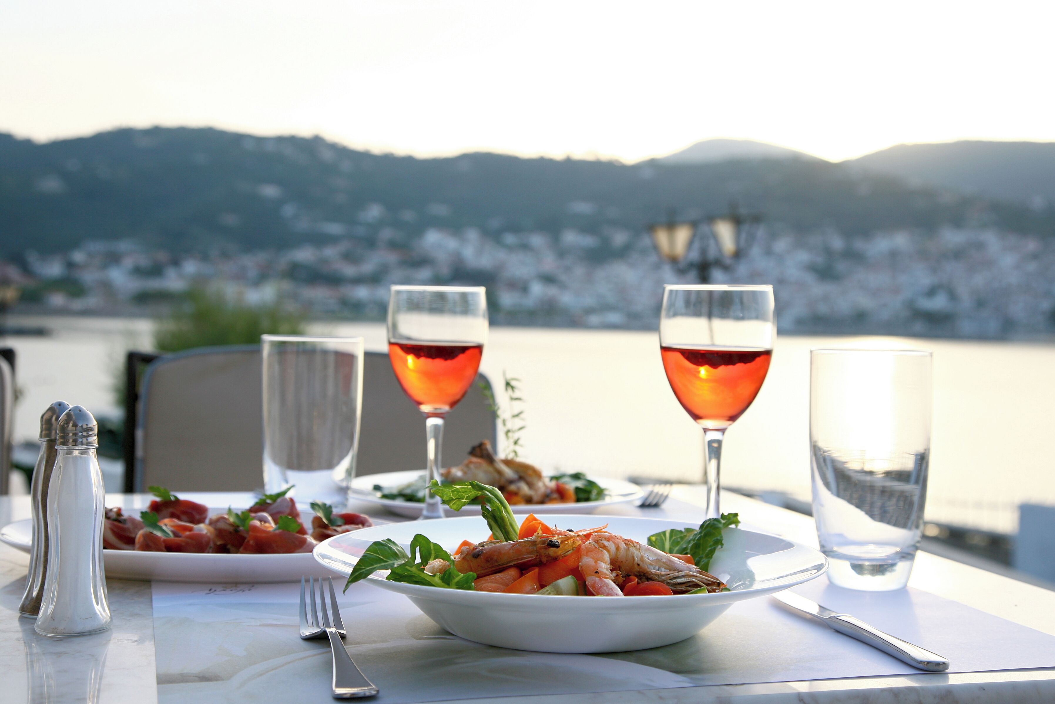 Une table avec une assiette de nourriture, deux verres de vin rouge et un verre d’eau.
