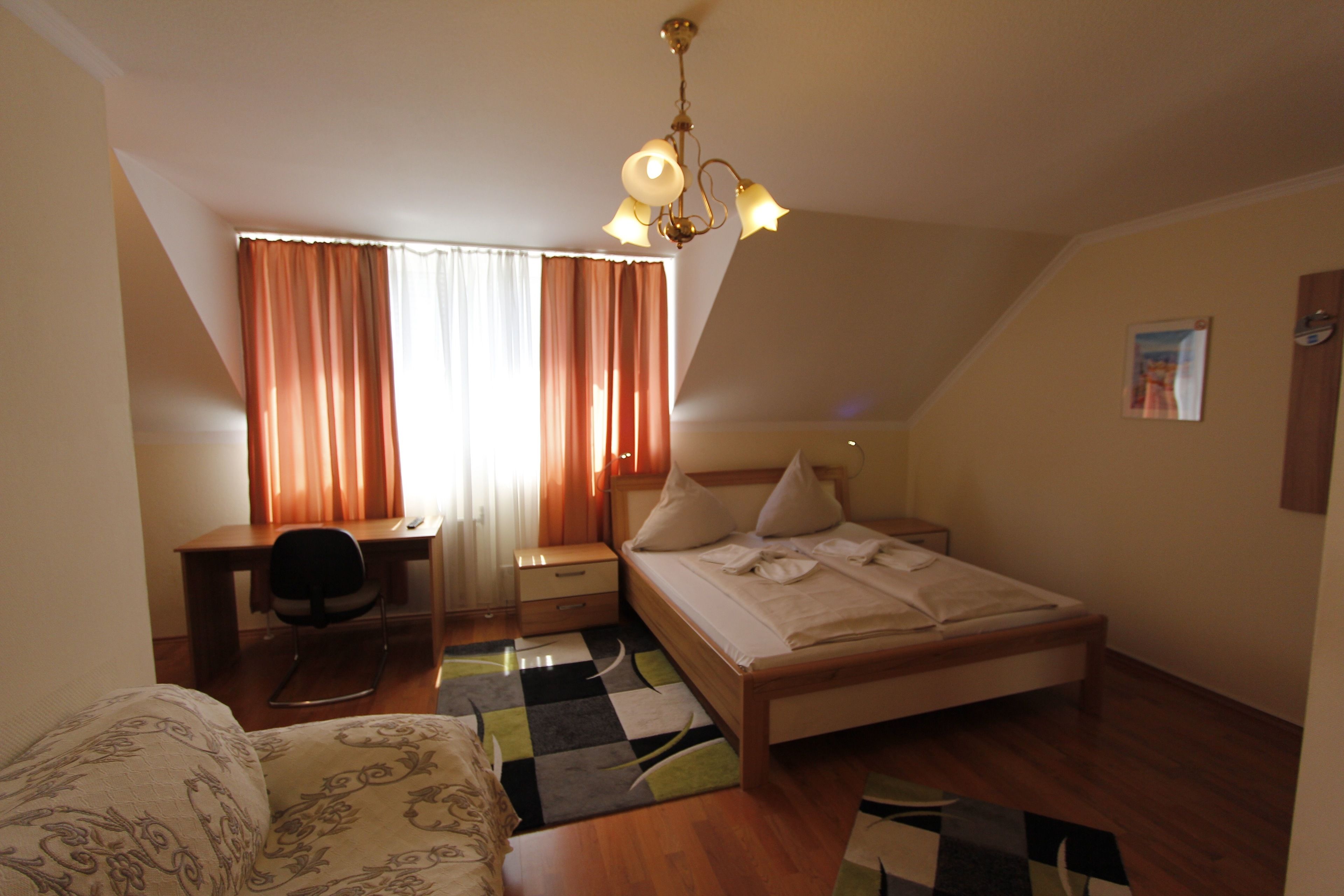 A bedroom with a bed, a desk, a chair, and a window with curtains.