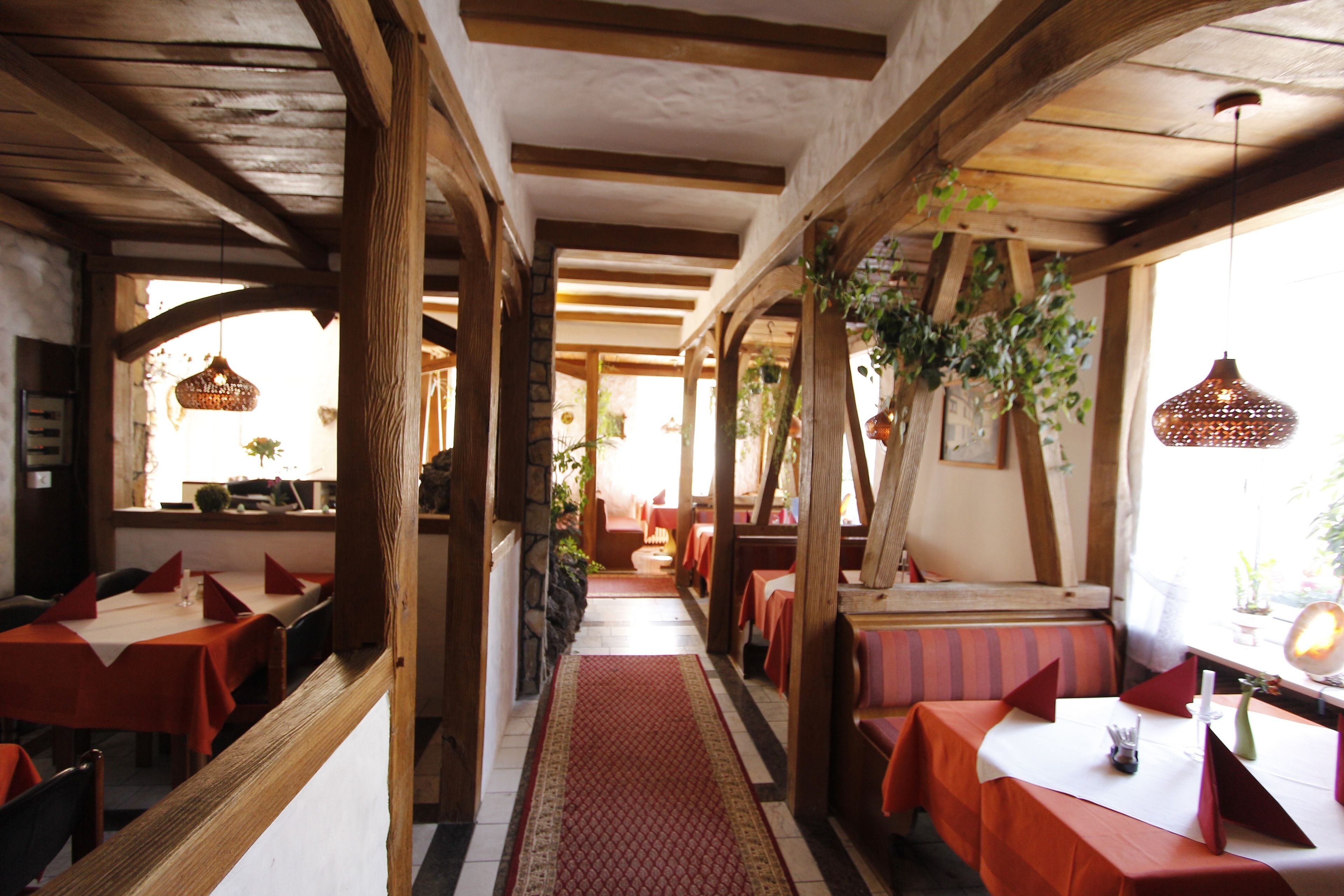 A restaurant with wooden beams, red tablecloths, and hanging plants.