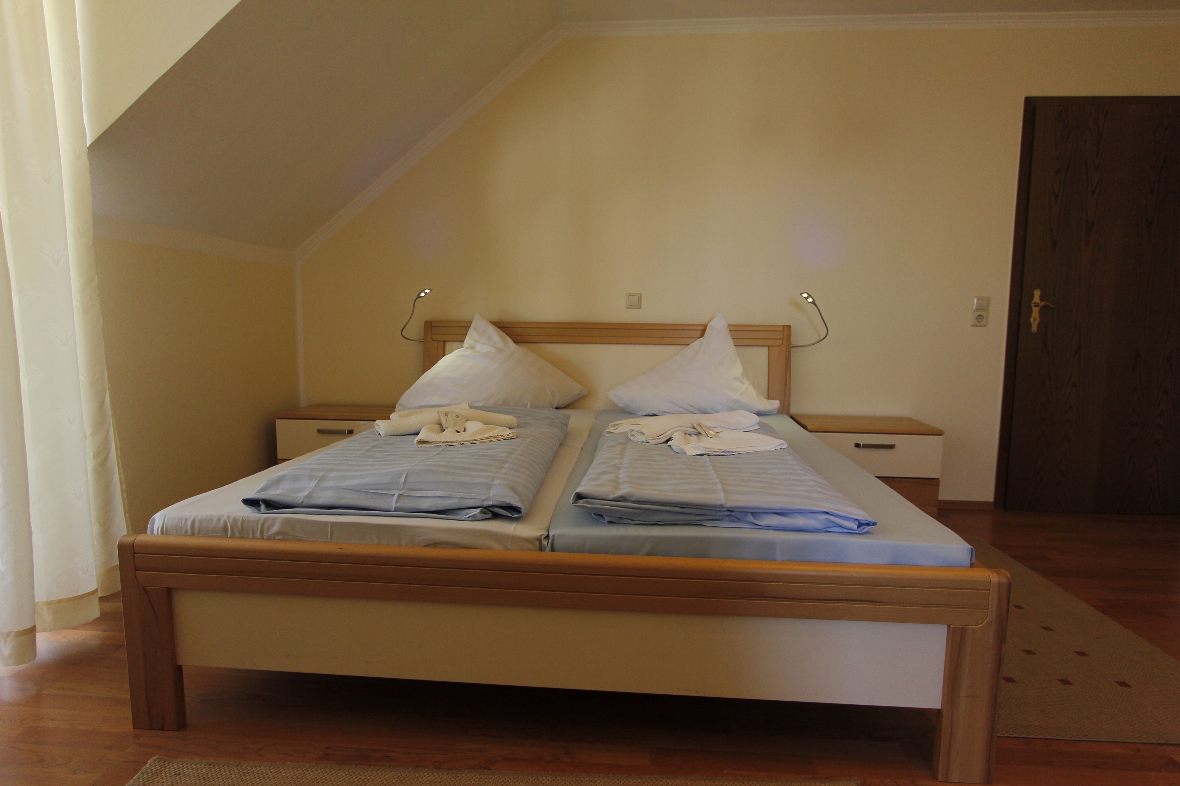 A double bed with two pillows and a folded towel, wooden headboard, bedside tables, and a door.