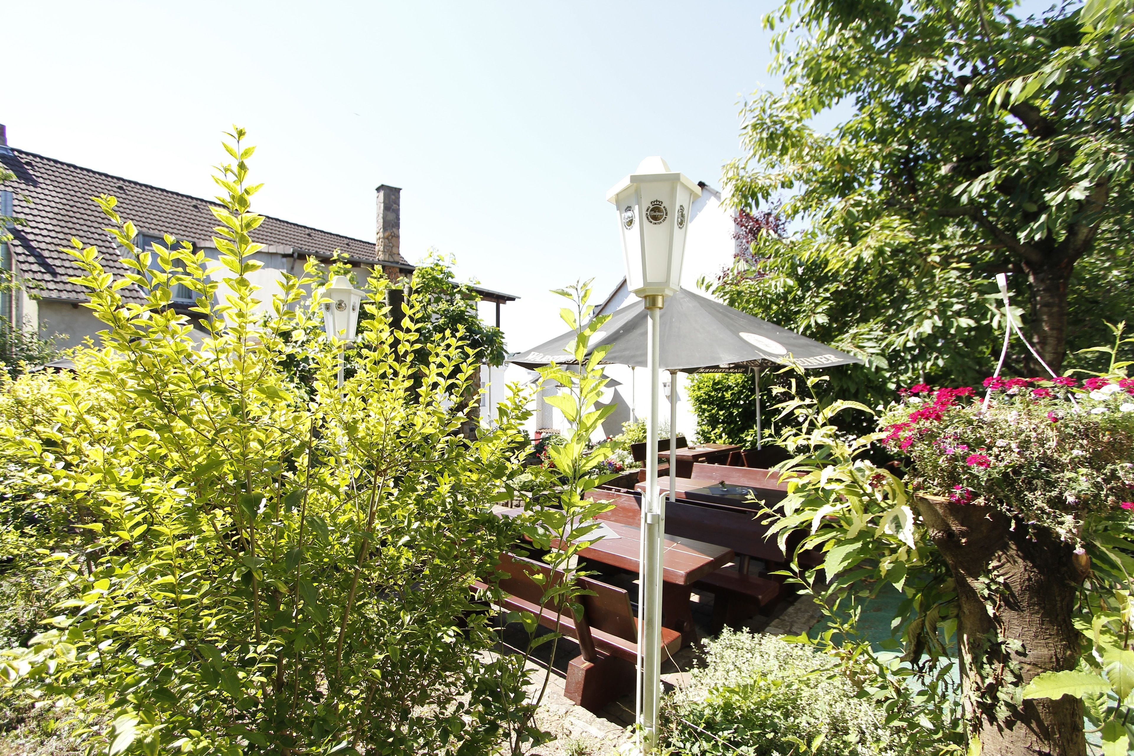 Un jardín con un banco de madera, un farol blanco y una casa al fondo.