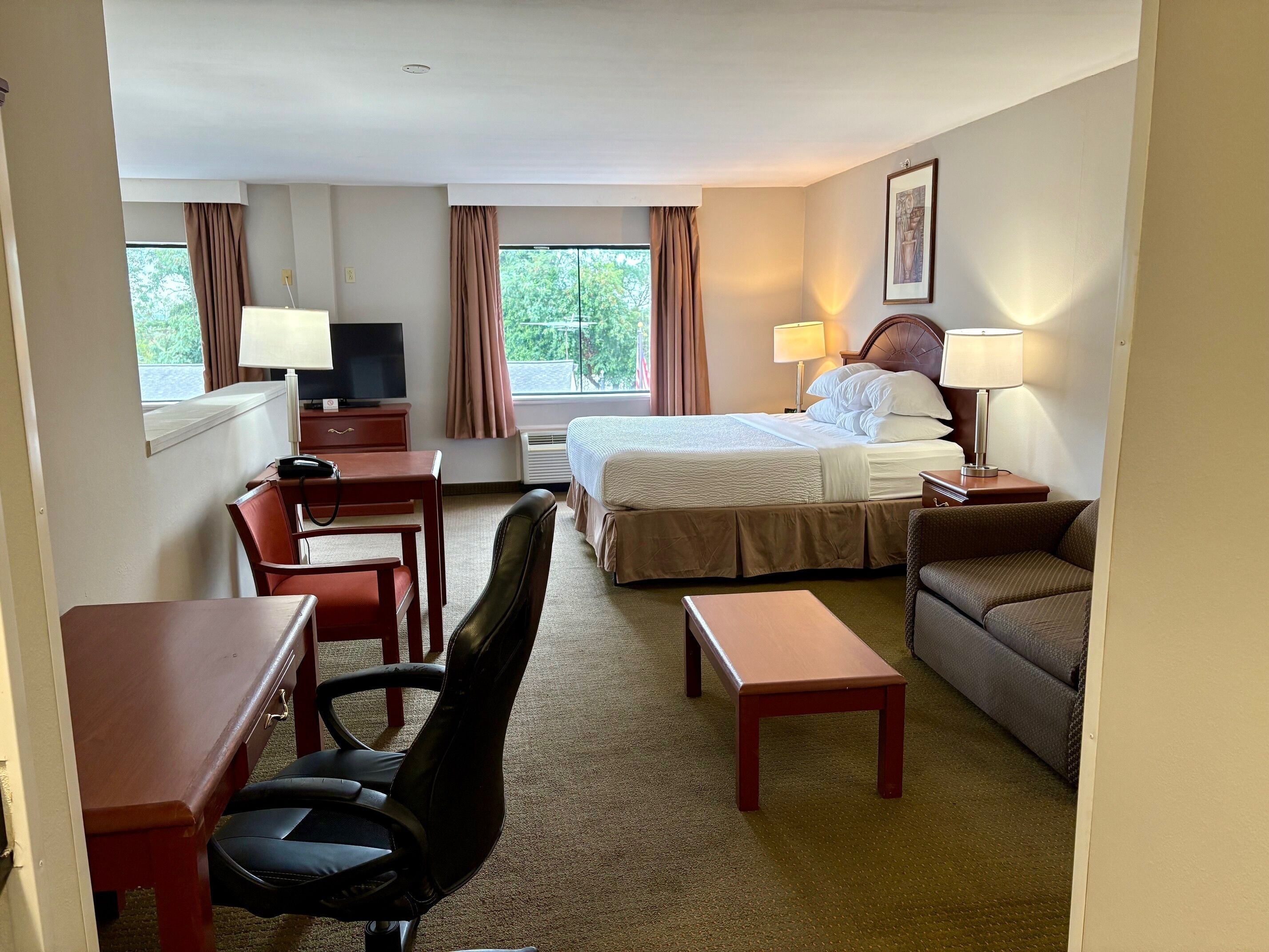 A hotel room with a bed, a desk, a chair, a sofa, and a TV.