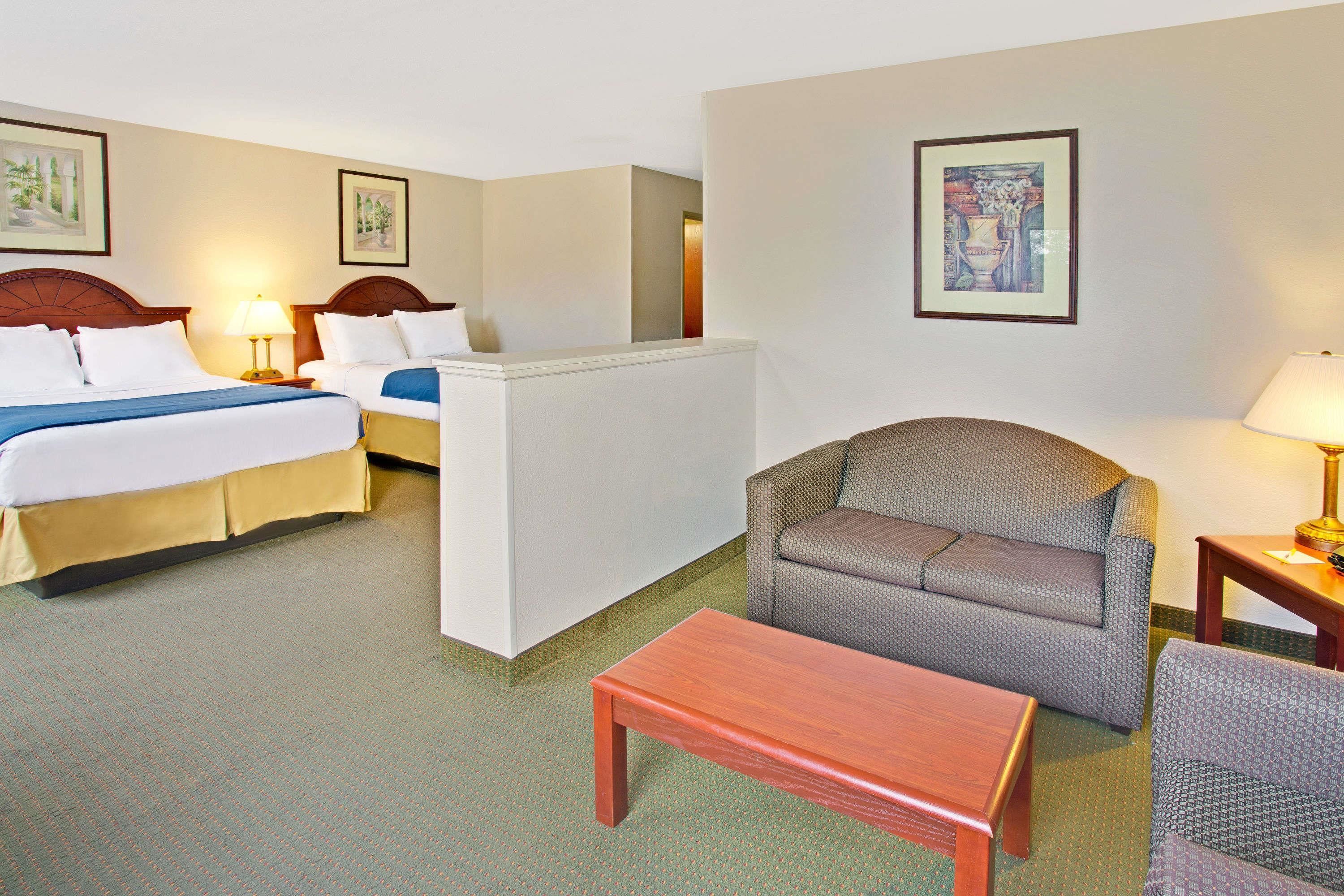 A hotel room with two beds, a sofa, a wooden table, and a chair.