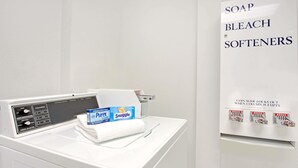A modern laundry machine with a control panel, a white towel, and detergent boxes labeled "Purex" and "Snuggle". - Days Inn & Suites by Wyndham Laurel Near Fort Meade (Laurel)