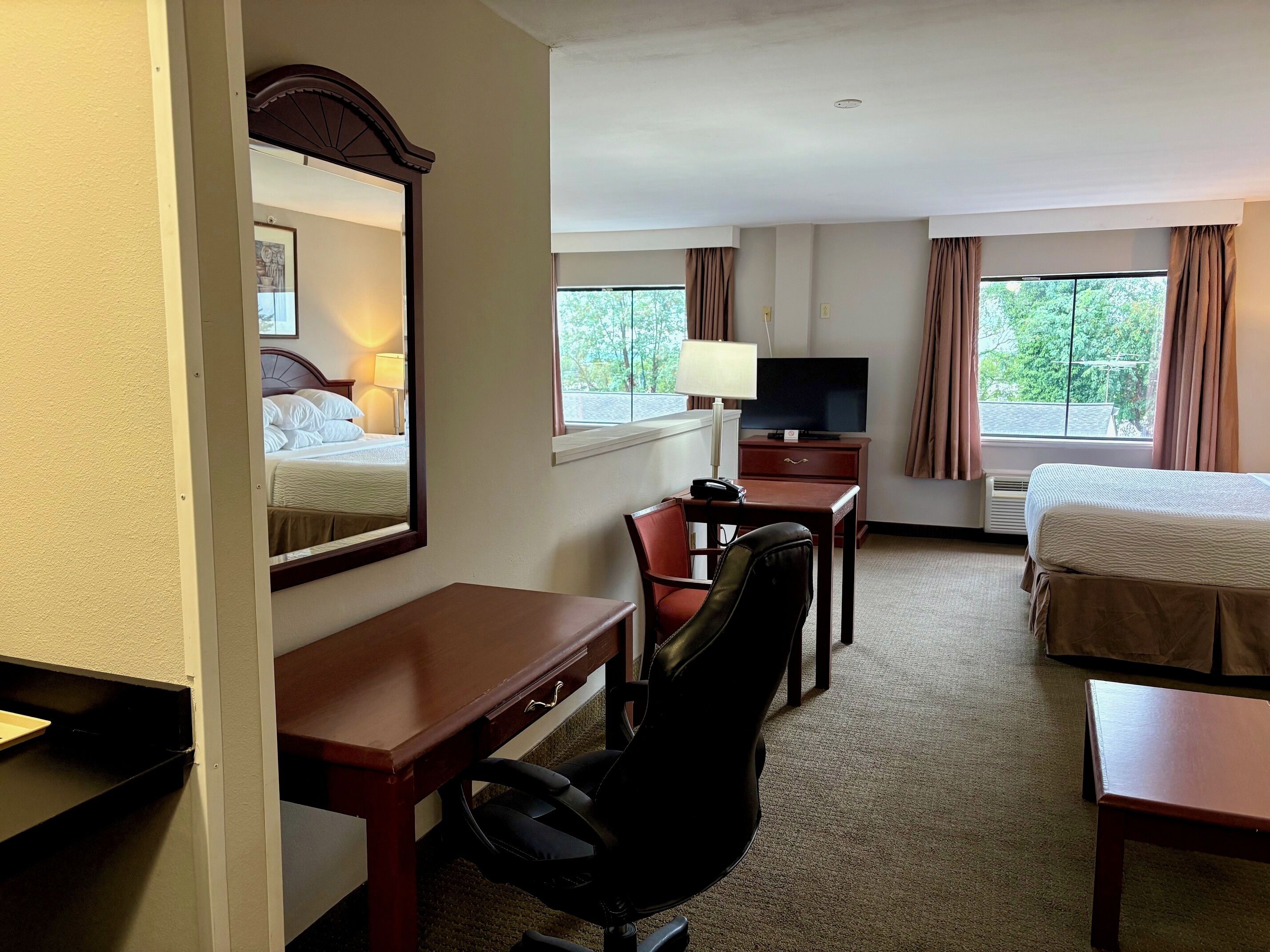 A hotel room with a bed, a desk with a chair, a television, and a window with curtains.