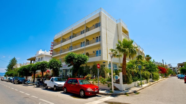 Um hotel com vários andares, varandas, estacionamento e palmeiras.