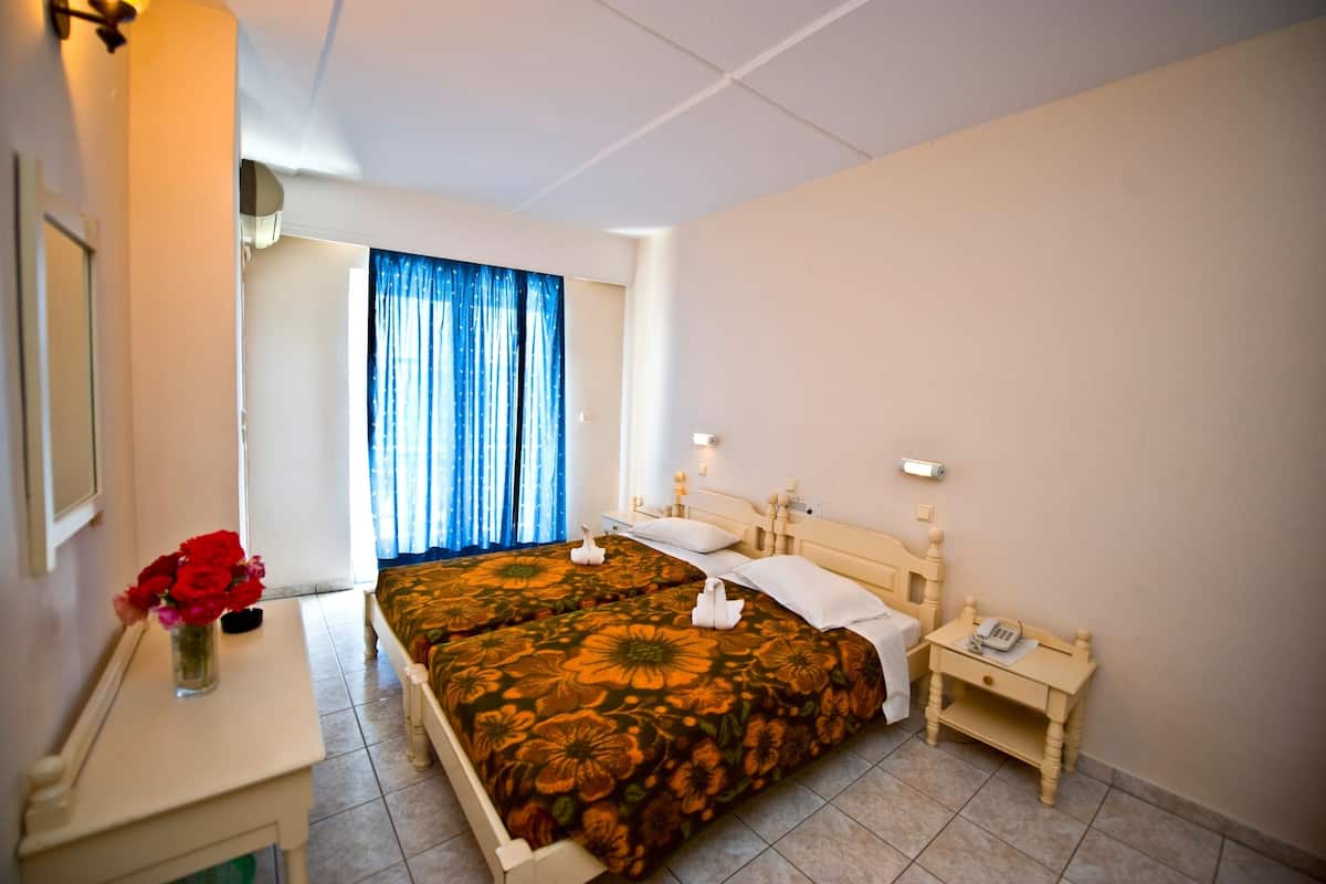 A hotel room with two beds, a bedside table with a phone, and a vase with red flowers.