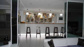 A modern living room with a bar area, featuring a sofa, bar stools, and a variety of bottles on shelves.