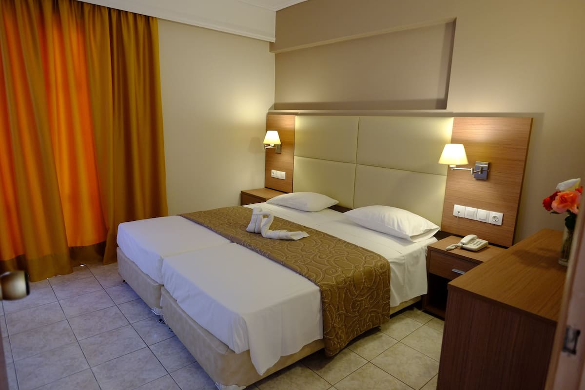 A hotel room with a double bed, two bedside tables with lamps, a wooden headboard, and a nightstand with a phone.