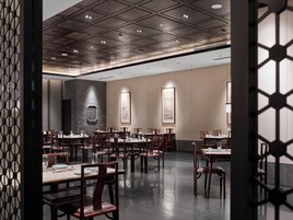 A restaurant with multiple tables and chairs, a patterned ceiling, and traditional artwork on the walls.
