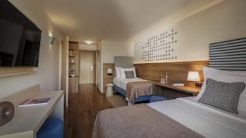 A hotel room with two beds, a desk, a chair, a bedside table with a lamp, and a wall with a circular pattern.
