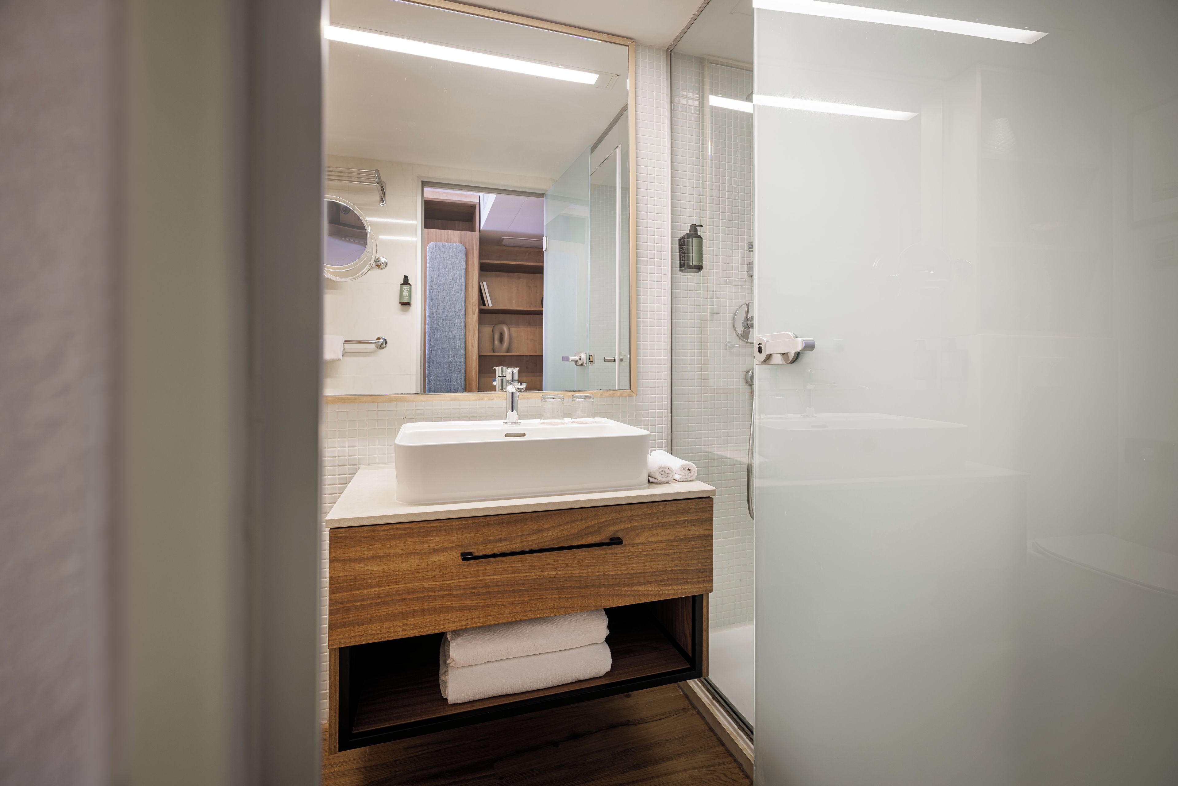 A modern bathroom with a white sink, wooden vanity, and a glass shower enclosure.