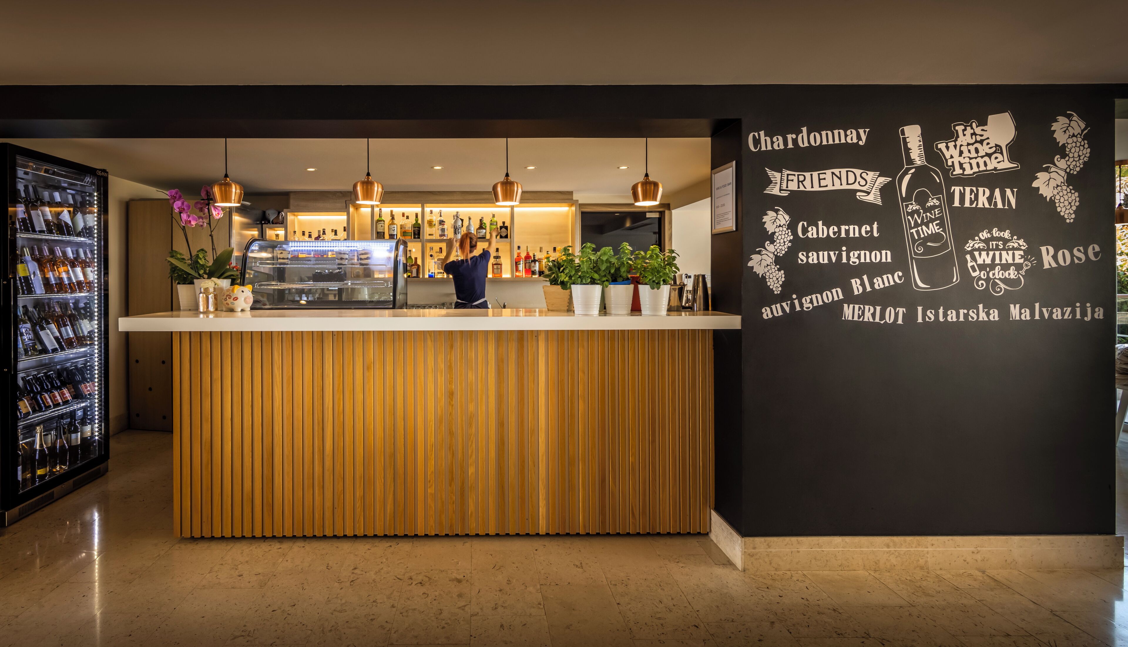 Zona de bar con mostrador de madera, luces colgantes y una pared con nombres de vinos.