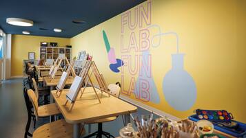 Un aula con mesas, sillas y material de arte, con una pared que muestra la inscripción 'FUN LAB FUN'.
