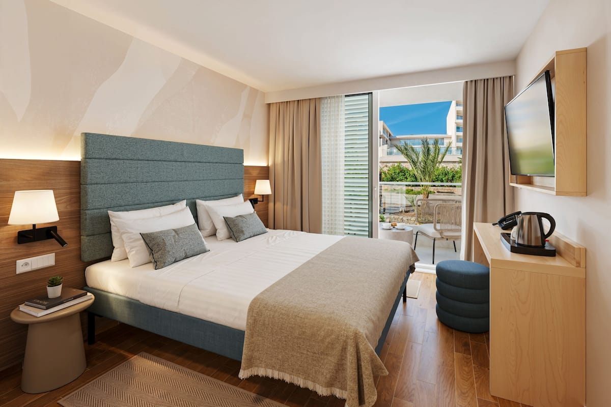 Una habitación de hotel moderna con una cama grande, un escritorio, un televisor y vistas al exterior.