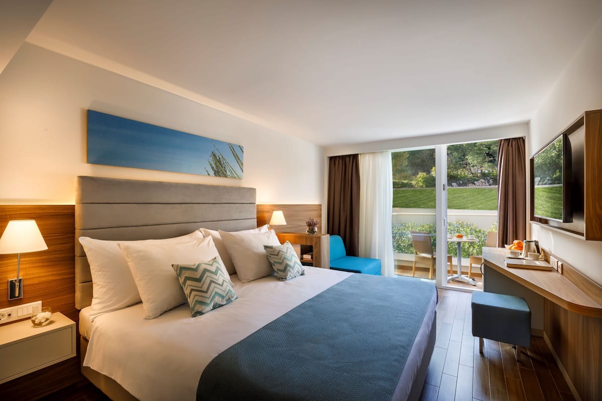 Una habitación de hotel con una cama grande, un escritorio y un balcón con vistas al jardín.