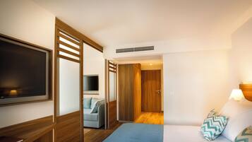 A hotel room with a bed, a TV, a wardrobe, and a door leading to another room.
