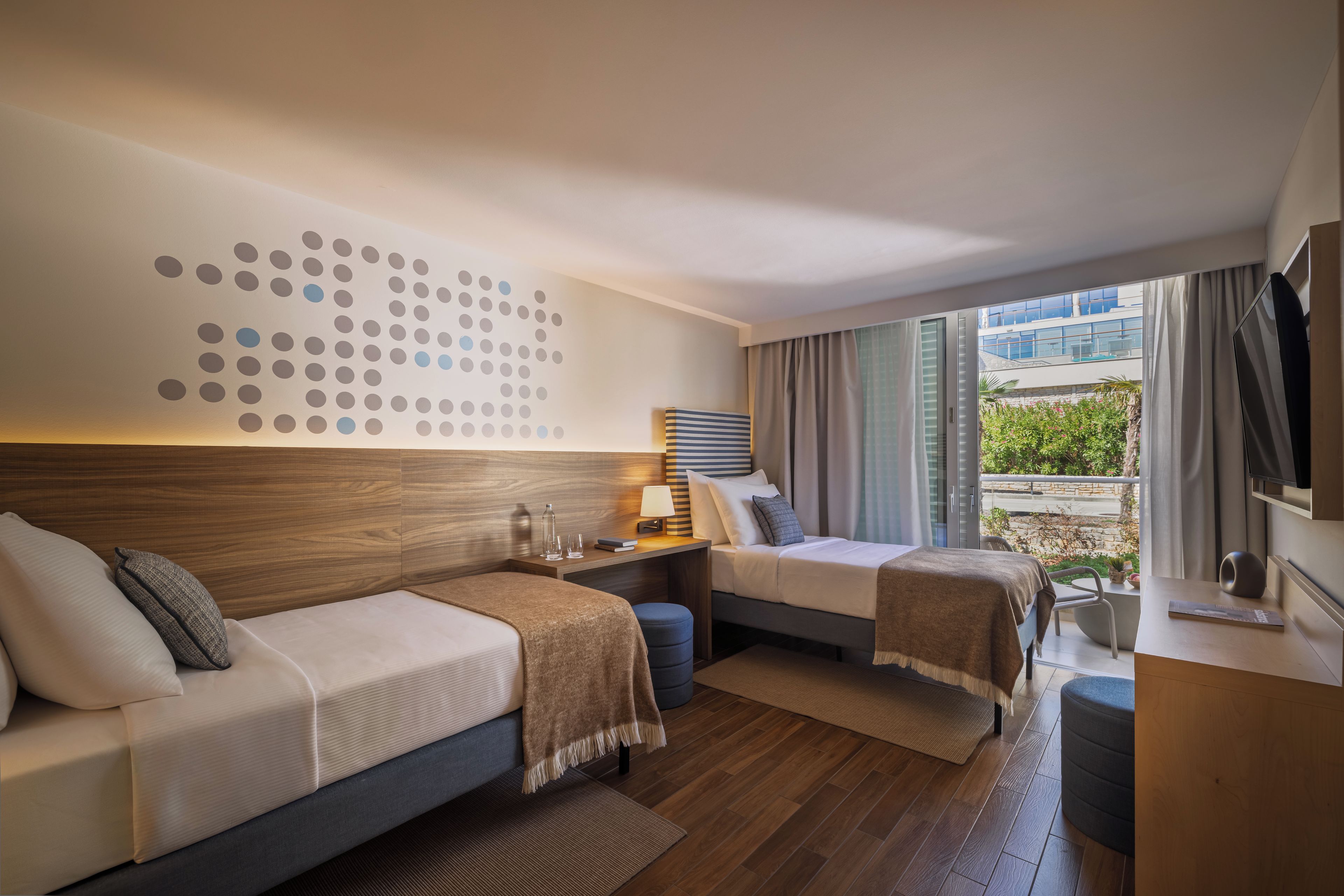 A modern hotel room with a large window, a bed, a desk, and a seating area.