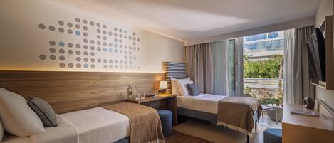 A modern hotel room with a large window, a bed, a desk, and a seating area.