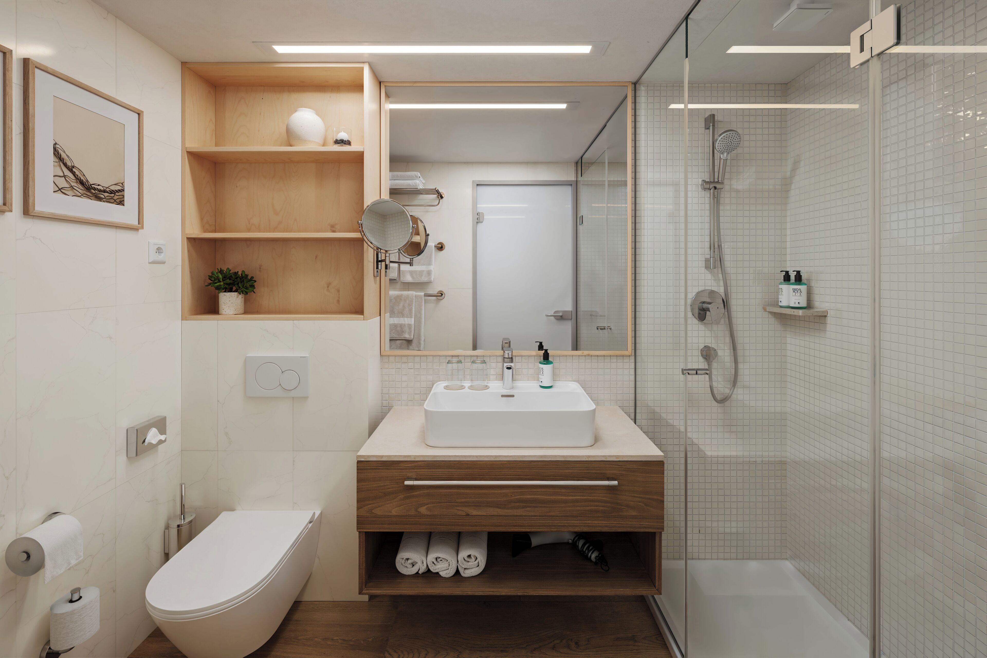 A modern bathroom with a freestanding toilet, a sink with a mirror, a shower area, and a wooden vanity.