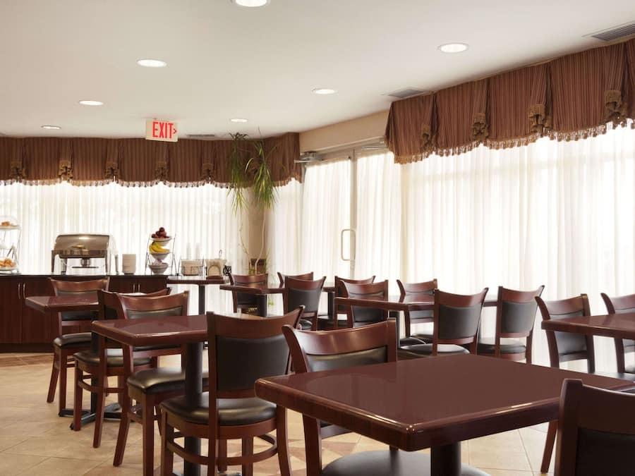 A dining area with multiple tables and chairs, an exit sign, and a buffet counter with food items.