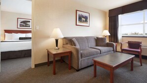 A hotel room with a bed, a grey sofa, a wooden coffee table, two side tables with lamps, a chair, and framed pictures on the wall. - Days Inn & Suites by Wyndham Langley (Langley)