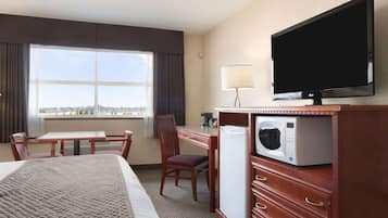 A hotel room with a bed, a desk, a chair, a television, a microwave, and a window with a view.