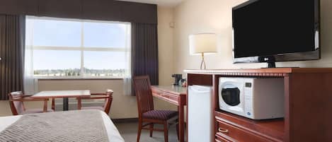 Habitación de hotel con cama, escritorio, silla, televisión, microondas y ventana con vista.