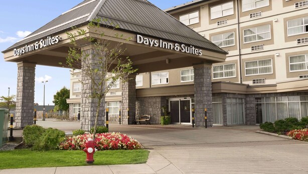 A Days Inn & Suites building with a stone facade, a covered entrance, and a landscaped entrance area with flowers and a fire hydrant. - Days Inn & Suites by Wyndham Langley (Langley)