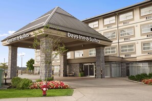 A Days Inn & Suites building with a stone facade, a covered entrance, and a landscaped entrance area with flowers and a fire hydrant.
