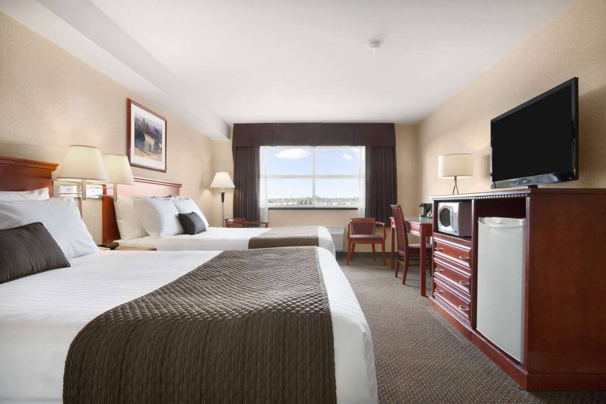 Habitación de hotel con dos camas, un escritorio con silla, televisión, microondas y refrigerador.
