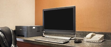 A hotel reception desk with a desktop computer, a printer, a telephone, and a black office chair.