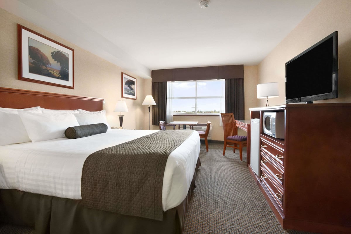 Habitación de hotel con una cama grande, un escritorio con silla, un televisor y ventana con vistas.