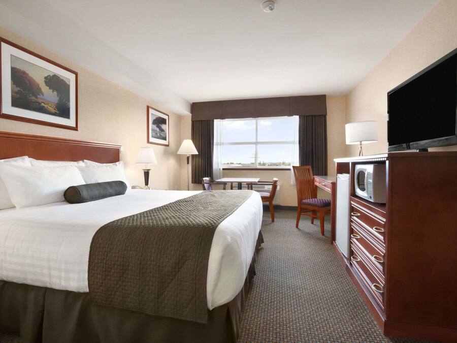 A hotel room with a large bed, a desk with a chair, a television, and a window with a view.