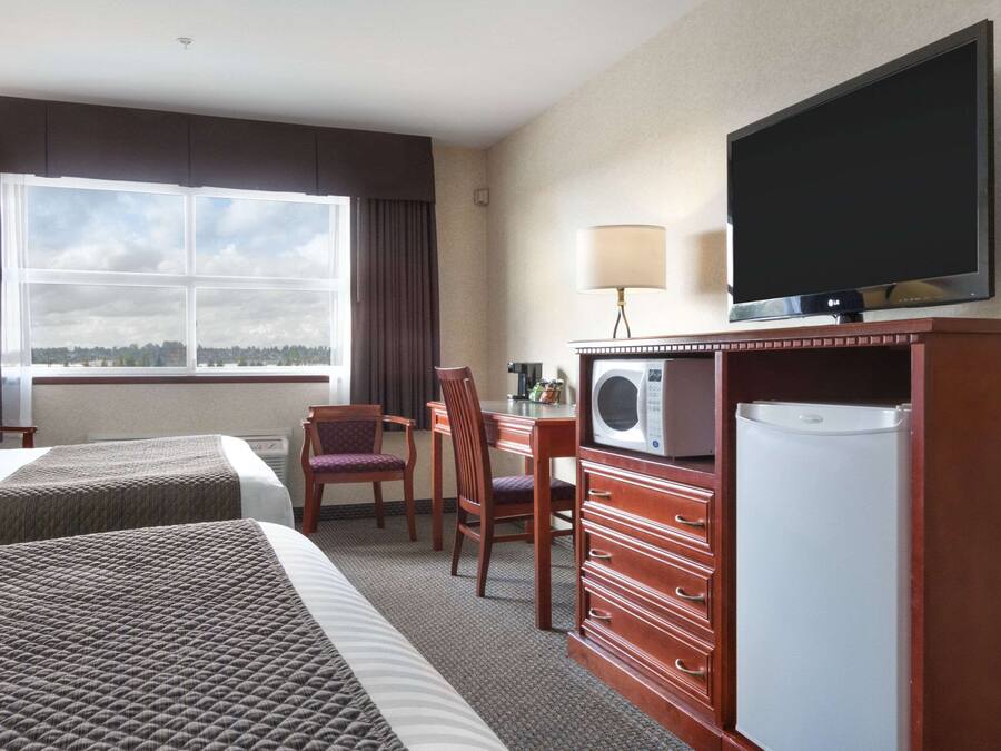 A hotel room with two beds, a desk with a chair, a television, a microwave, and a refrigerator.