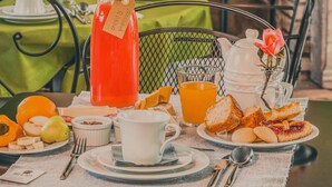 Een ontbijtsetting met een tafel voor twee personen, met een karaf sinaasappelsap, een theepot en diverse ontbijtartikelen zoals brood, fruit en gebak.