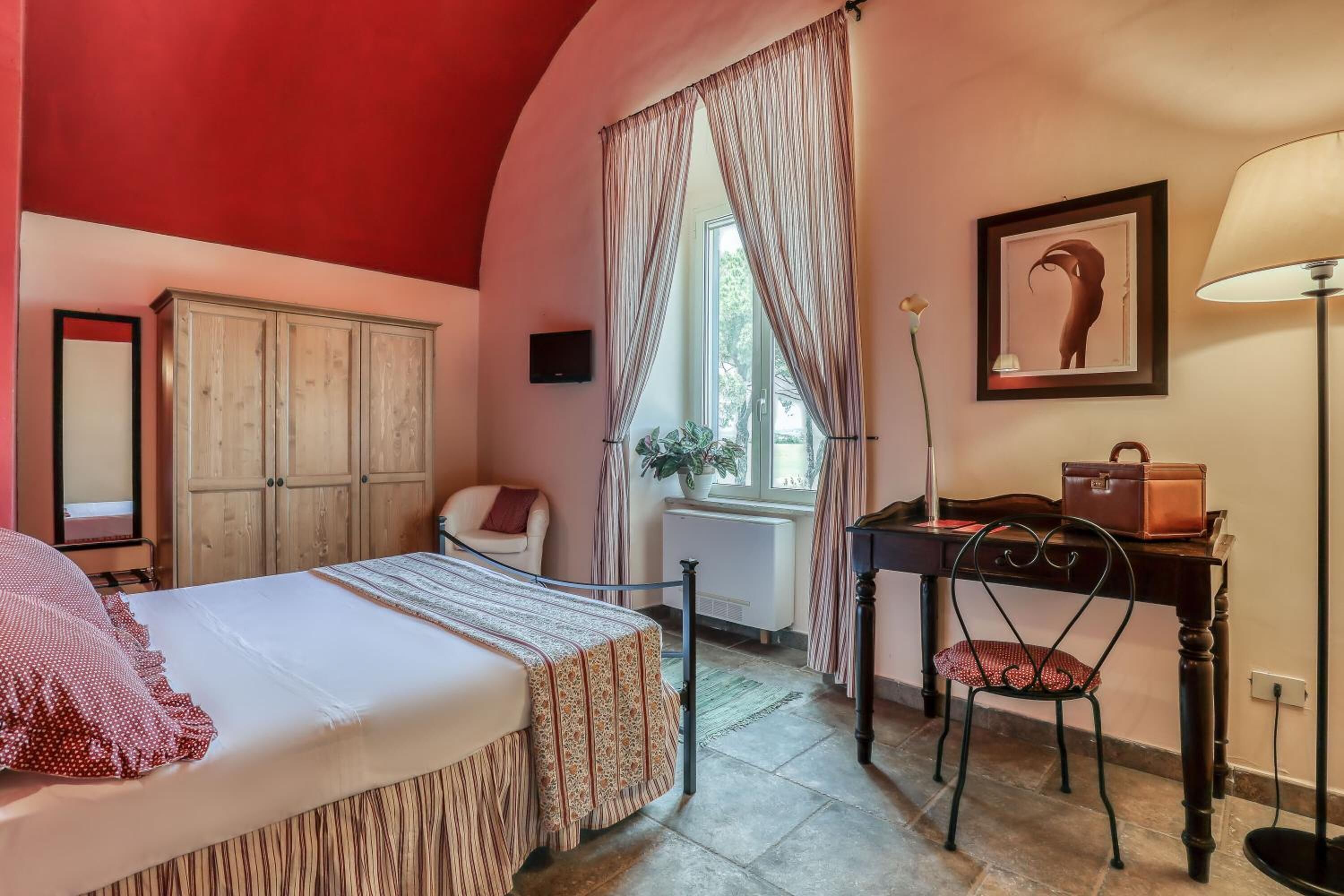 Una habitación con cama, escritorio, silla, armario, ventana con cortinas y lámpara.
