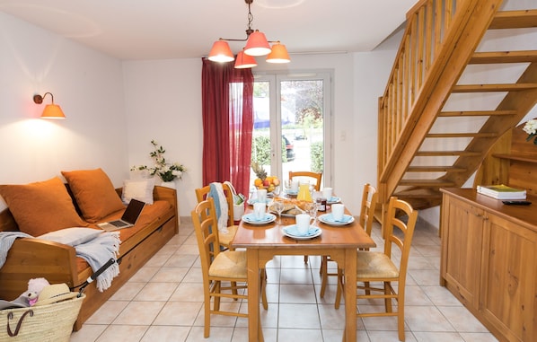 A cozy living room with a wooden sofa, a dining table set for four, and a wooden staircase.