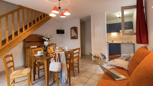 A cozy living space with a wooden staircase, a dining area with a table set for two, a kitchen with a microwave, and a laptop on a couch. - Odalys Residence Coeur d’Ardèche (Vallon-Pont-d'Arc)