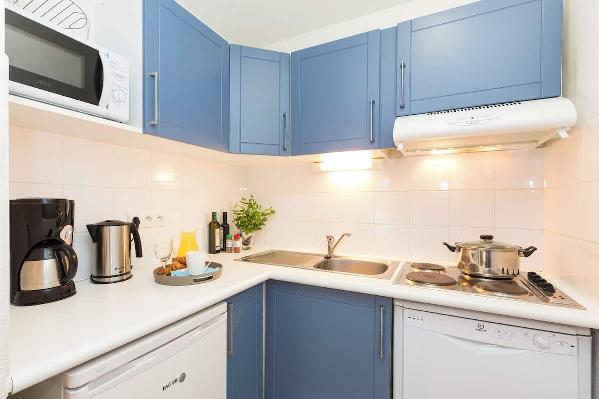 Una cocina moderna con armarios azules, un microondas, una cafetera, un hervidor, un fregadero y una estufa.