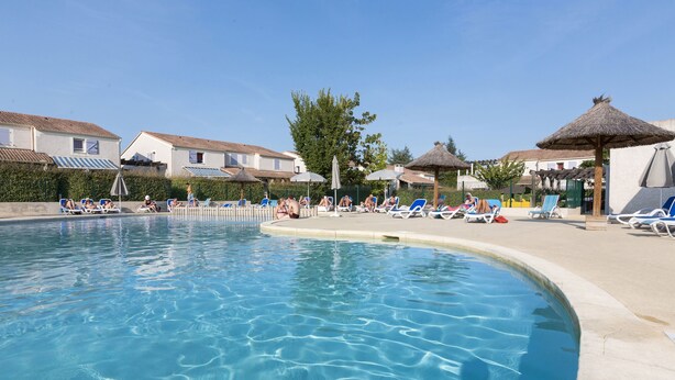 A swimming pool with lounge chairs and umbrellas, surrounded by buildings with a consistent architectural style. - Odalys Residence Coeur d’Ardèche (Vallon-Pont-d'Arc)