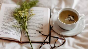 Un livre ouvert, une tasse de thé et une paire de lunettes posés sur une surface blanche.