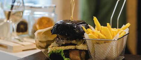 A burger with fries on a black plate, a glass of water, and a vase with a plant in the background.